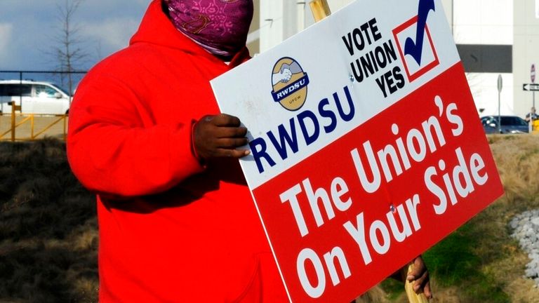 FILE - In this Tuesday, Feb. 9, 2021, file photo, Michael Foster of the Retail, Wholesale and Department Store Union holds a sign outside an Amazon facility where labor is trying to organize workers in Bessemer, Ala. Nearly 6,000 Amazon warehouse workers in Bessemer, Alabama, have voted on whether or not to form a union. But the process to tally all the ballots and determine an outcome will continue for a second week, according to the National Labor Relations Board, a government agency that’s co