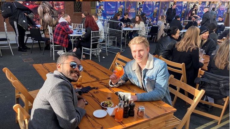 People sit at tables outside pubs, bars and restaurants in London's Soho