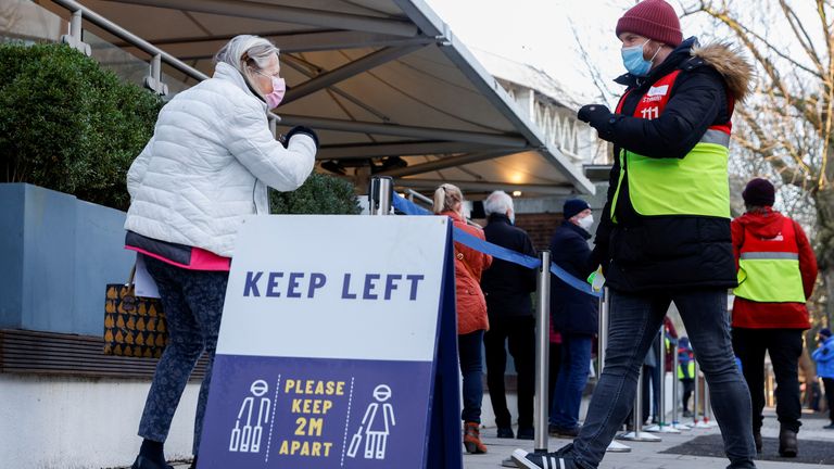A woman wearing a protective mask is greeted by a member of staff as she joins the queue for vaccinations at Lord's Cricket Ground