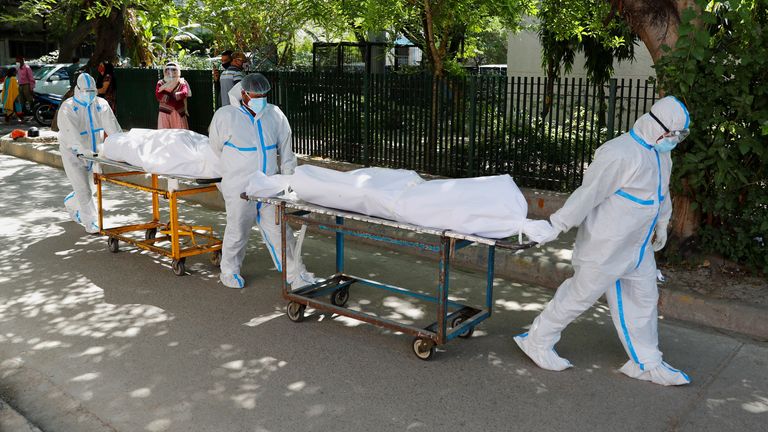 کارکنان بهداشتی که از تجهیزات حفاظت شخصی (PPE) استفاده می کنند اجساد را حمل می کنند 