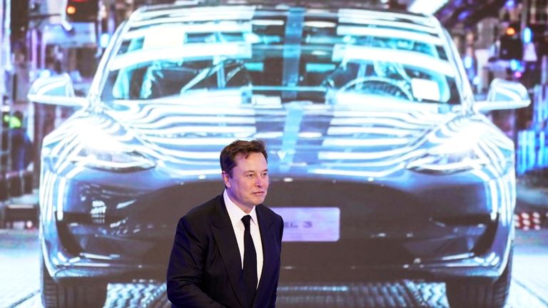 Elon Musk walks next to a screen showing an image of Tesla Model 3 car during an opening ceremony for its China-made Model Y