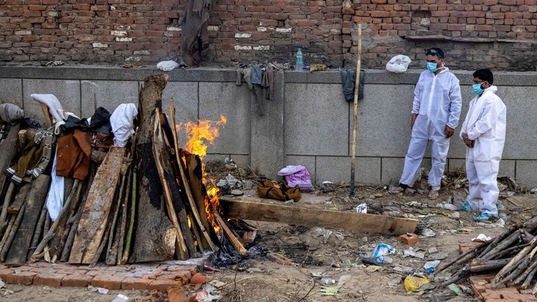 Relatives stand next to the burning funeral pyre at a crematorium ground in New Delhi