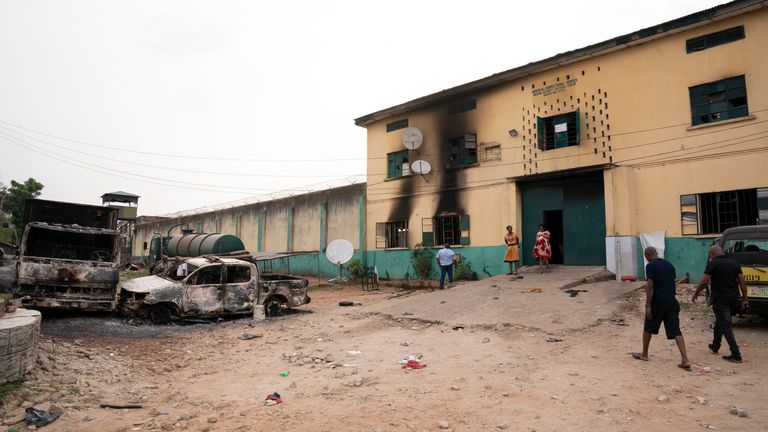 People walk past Burnt cars in front of a Nigerian correctional services  in Owerri, following gunmen attack in Nigeria, Monday