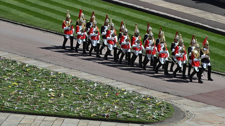 Military in parade dress uniform march past flowers. Pic: AP