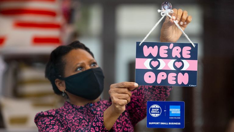 Owner Isatu Funna from Dar Leone displays a "we&#39;re open" sign designed by artist Timothy Hunt, which has been created as part of the American Express Shop Small campaign and to help welcome people back to our high streets