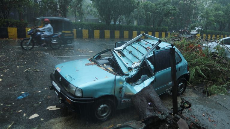 A damaged car is seen on a road after a tree fell on it due to strong winds caused by Cyclone Tauktae