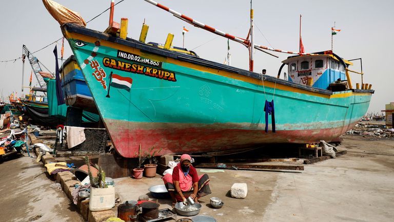 زنی به دنبال طوفان Tauktae در واناکبارا در دیو هند در کنار قایق های صیادی پهلو غذا تهیه می کند