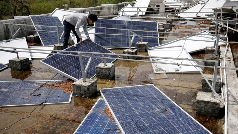 A man assesses damage to solar panels on a building in Diu