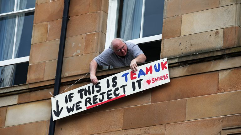A man holds a protest sign on Kenmure Street