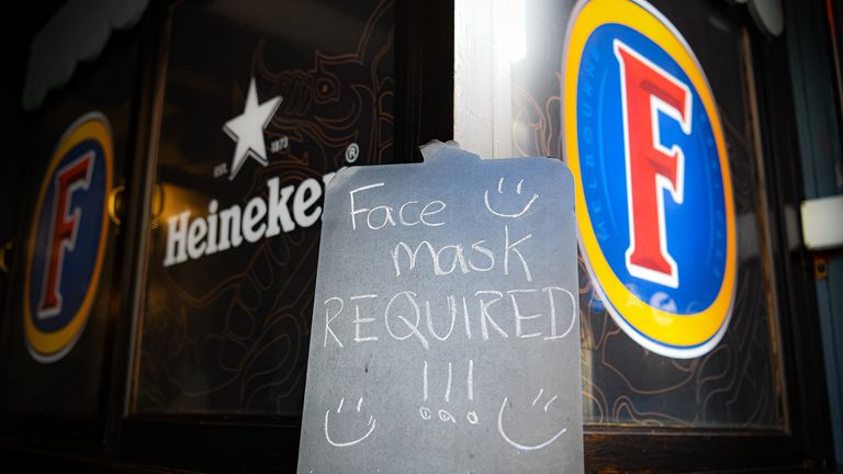 A face mask requirement sign beside alcohol branding at a pub in Cardiff