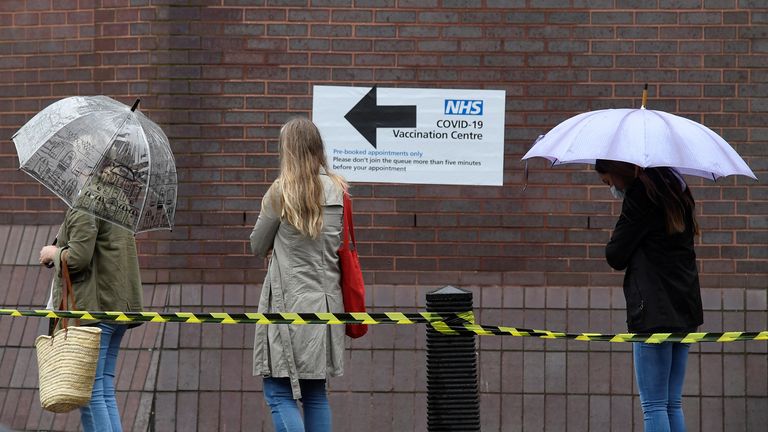 People queue in the rain to receive a COVID-19 vaccination