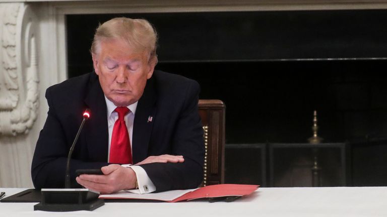 U.S. President Donald Trump uses a mobile phone as Oklahoma Governor Kevin Stitt is seated nearby during a roundtable discussion on the reopening of small businesses in the State Dining Room at the White House in Washington, U.S., June 18, 2020. REUTERS/Leah Millis
