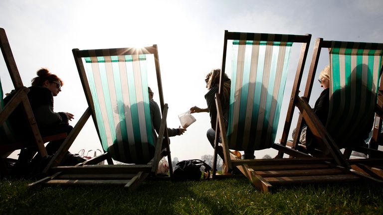 Tourists have a picnic in the park as they sit in the sun in deck chairs in Hyde Park, London