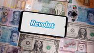 A smartphone displays a Revolut logo on top of banknotes