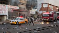 A woman walks past a fire engine as it extinguishes flames in a looted store in Alexandra township, Johannesburg. Pic: AP
