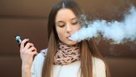 Vape teenager. Young pretty white girl in casual clothing smoking an electronic cigarette opposite modern brown background on the street in the spring. Bad habit. Vaping activity. Close up.