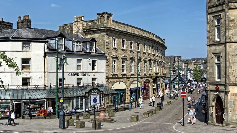 View of Buxton town centre, Derbyshire, UK.  Shops can be seen on the far side of the road and people can be seen waking on the pavements.