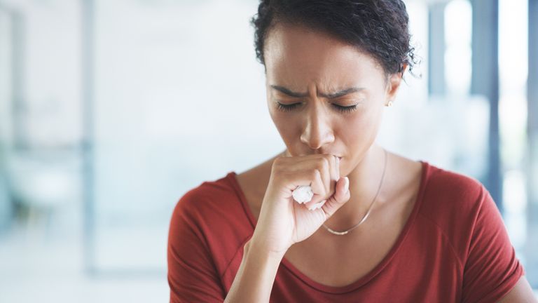 Cropped shot of an young businesswoman sitting alone in her office and coughing as she suffers from a cold