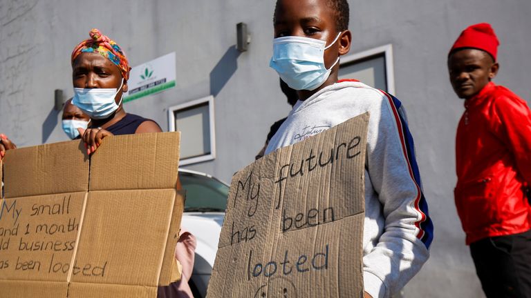 People stand with placards as Cyril Ramaphosa visited a Durban shopping centre damaged in the riots that followed the imprisonment of former leader Jacob Zuma