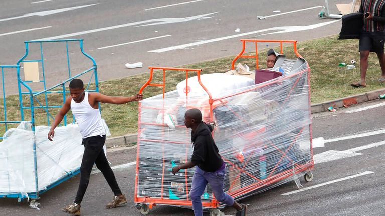 People make their way with good on a trolley taken from a store in Durban, South Africa, Tuesday July 13, 2021