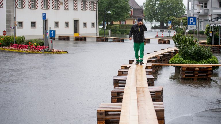 Une personne marche sur une passerelle alors que la place du village est couverte d'eau de crue à Stansstad.  Photo : AP
