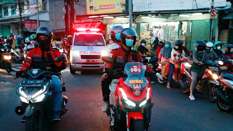 Volunteer bikers escort an ambulance to a cemetery in Jakarta
