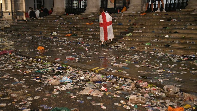 An England fan draped in a flag walks amongst the litter strewn on the ground in front of St Martin-In-The-Fields church, in Trafalgar Square, London, after Italy beat England on penalties to win the UEFA Euro 2020 Final. Picture date: Sunday July 11, 2021.