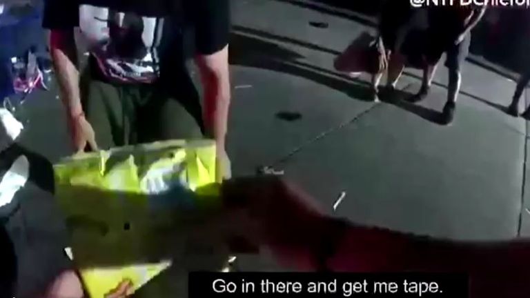 The police officer flattens a crisps bag before instructing a bystander to get tape