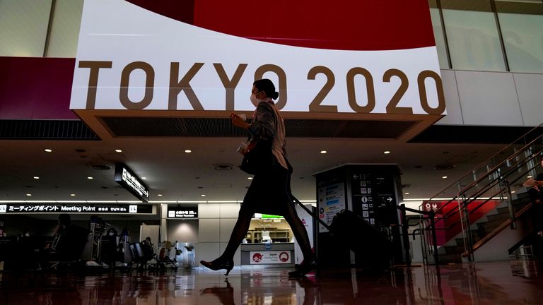 A flight attendant walks by a large display of Tokyo 2020 Olympics at Narita International Airport Thursday, July 15, 2021, in Narita, east of Tokyo. (AP Photo/Kiichiro Sato)