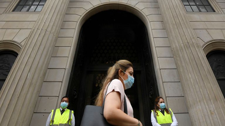 A worker wearing a protective face mask walks past the Bank of England in the City of London