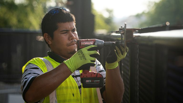 A worker is seen removing bolts from the fence with a drill