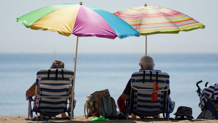 People sit under umbrallas as they enjoy the hot weather at Bournemouth Beach in Dorset