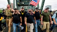 organizer Joe Biggs, in green hat, and Proud Boys Chairman Enrique Tarrio, holding megaphone, march with members of the Proud Boys and other right-wing demonstrators march across the Hawthorne Bridge during a rally in Portland