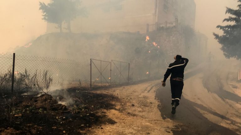 A civil protection rescue worker walks near smoke rising from a forest fire in the mountainous Tizi Ouzou province, east of Algiers, Algeria August 10, 2021. REUTERS/Abdelaziz Boumzar