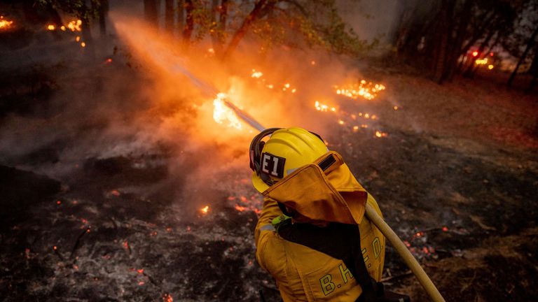 A firefighter hoses down flames from the Dixie Fire in Genesee, California, 21 August. Pic: AP