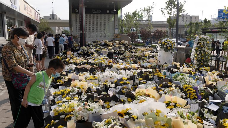 Des gens se tiennent à côté de fleurs placées à l'entrée d'une station de métro de la ligne 5 du métro à la mémoire des victimes des inondations à la suite de fortes pluies à Zhengzhou, dans la province du Henan, en Chine, le 27 juillet 2021. Photo prise le 27 juillet 2021. China Daily via REUTERS ATTENTION EDITORS - CETTE IMAGE A ÉTÉ FOURNIE PAR UN TIERS.  EN CHINE.