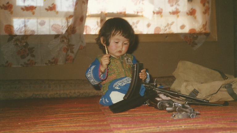 Homira plays with an AK47 as a toddler growing up in Afghanistan