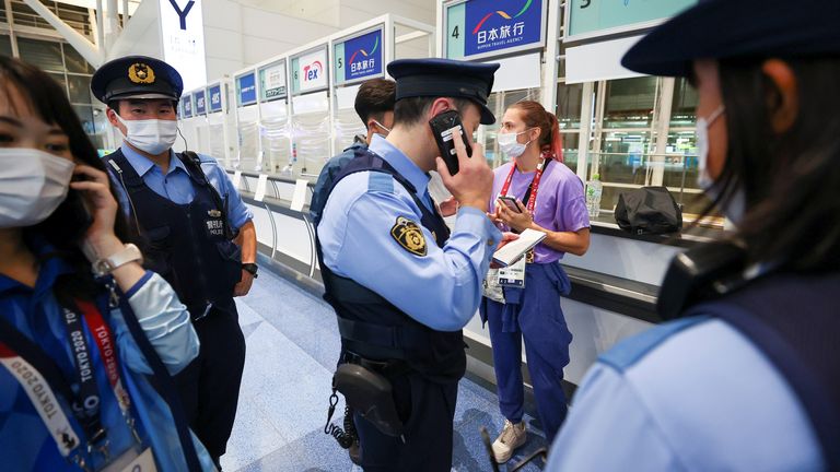 Belarusian athlete Krystsina Tsimanouskaya stands surrounded by police officers at Haneda international airport in Tokyo, Japan