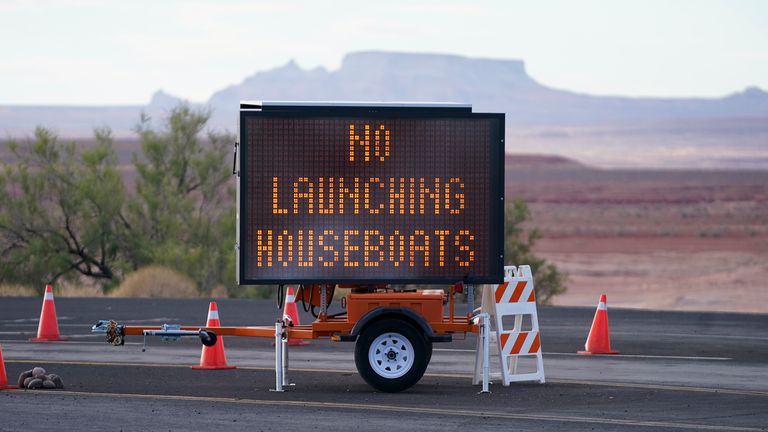 A "NO LAUNCHING HOUSEBOATS" sign is shown at the Wahweap launch ramp on Lake Powell Saturday, July 31, 2021, near Page, Ariz. This summer, the water levels hit a historic low amid a climate change-fueled megadrought engulfing the U.S. West. Closed boat ramps have forced some houseboats off the water, leaving tourists and businesses scrambling. (AP Photo/Rick Bowmer)