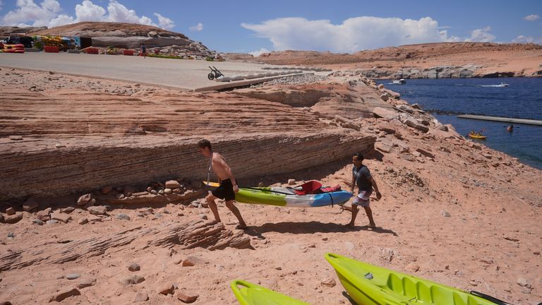 Visitors carry a kayak up a newly exposed cliff face beneath the closed Antelope Point launch ramp on Lake Powell Saturday, July 31, 2021, near Page, Ariz. This summer, the water levels hit a historic low amid a climate change-fueled megadrought engulfing the U.S. West. (AP Photo/Rick Bowmer)