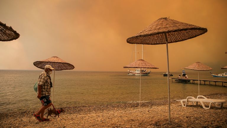 A man walks with his dog on the beach of smoke-engulfed Mazi area as wildfires rolled down the hill toward the seashore, in Bodrum, Mugla, Turkey. Pic: AP