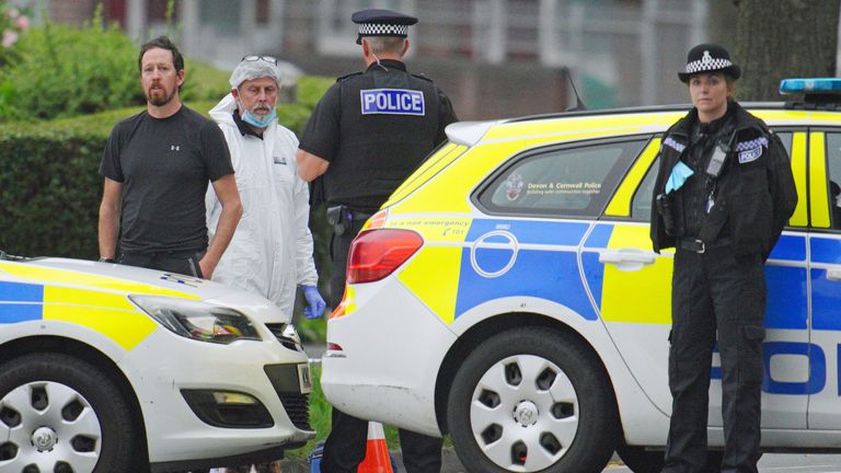 A police investigator alongside uniformed officers in Royal Navy Avenue near the scene where six people died of gunshot wounds