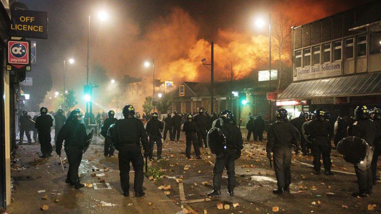 Riot police look on as smoke rises from burning buildings in Tottenham, north London