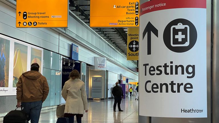 Travellers pass a sign for a COVID-19 test centre at Heathrow Airport