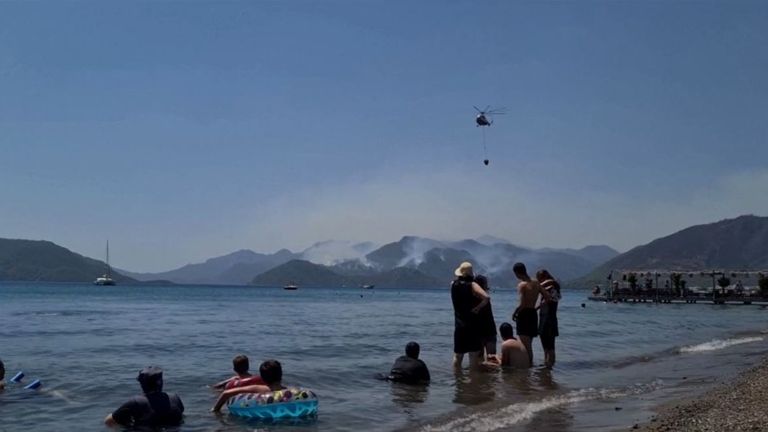 Helicopter flies over beachgoers in Marmaris, collecting water to combat wildfire 