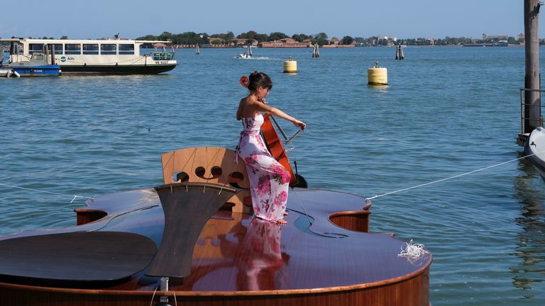 A musician plays a cello onboard a boat in the shape of a violin, titled &#39;Violin of Noah&#39;, that was built during the pandemic by artist Livio De Marchi in collaboration with Consorzio Venezia Sviluppo and is dedicated to people who have died from coronavirus, during a test-ride, in Venice, Italy, August 6, 2021. REUTERS/Manuel Silve