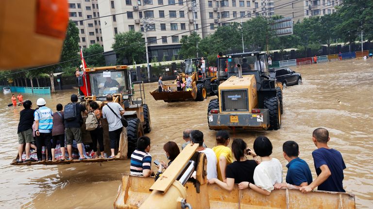 People ride on front loaders as they make their way through a flooded road following heavy rainfall in Zhengzhou, Henan province, China July 23, 2021. REUTERS/Aly Song