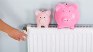 Person Hand Adjusting Thermostat With Two Piggy Banks On Radiator To Save Money At Home
ALAMY