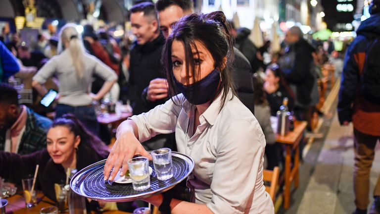 A waitress serves drinks at setup tables outside pubs in Soho, in London, on the day some of England&#39;s third coronavirus lockdown restrictions were eased by the British government, Monday, April 12, 2021. People across England flocked to shed shaggy locks and browse for clothes, books and other "non-essential" items as shops, gyms, hairdressers, restaurant patios and beer gardens reopened Monday after months of lockdown. (AP Photo/Alberto Pezzali)