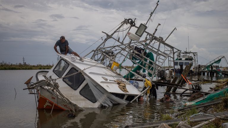 James Serigny climbs atop his sunken shrimp boat while getting help from friends to raise it, in the aftermath of Hurricane Ida in Golden Meadow, Louisiana, 